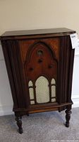 Front view of wooden cathedral-style console radio showing arched speaker grill and control knobs