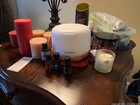 Photo showing 3 pillar jar candles in red and beige, essential oil diffuser, 3 essential oil bottles, white small jar candle with price sticker, box of tealight candles in plastic container.