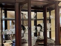 Glassware displayed inside a wooden and glass display cabinet showing various pitchers, bowls, and glasses with intricate designs and patterns.