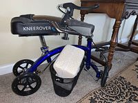 Side view of the blue KneeRover knee scooter showing the frame, knee pillow, carry basket, and rear wheels.
