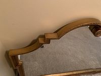 Close-up view of the stepped detailing on the gold metallic distressed frame and the edge of the mirror glass.