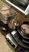 Photo showing nested stainless steel mixing bowls, dark metal baking pans and loaf pans stacked on shelves.