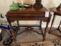 Front view of the antique wooden side table showing the rectangular top, turned legs, and carved apron.