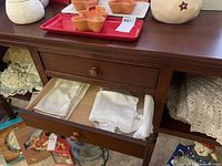 Doilies and linens arranged on a dark wooden shelf and inside an open drawer, showing folded white handkerchiefs and a variety of larger doilies and tablecloths stored on adjacent shelves.