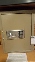 Front view of beige electronic wall safe closed with keypad and handle on the door.