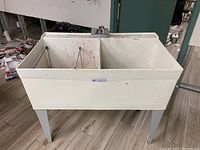Full view of white double laundry tub sink standing on four metal legs, stained with various paint colors from previous art room use.