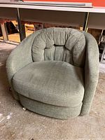 Front view of green barrel chair showing cushioned back with vertical stitching and rounded armrests.