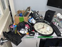 Wide shot of lot items on a table showing clock face, phone, mug with markers, push pins, and various wires and equipment