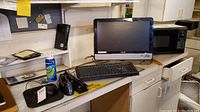 Computer desktop tower, all-in-one monitor, keyboard, mouse, microwave, and office supplies on a desk.