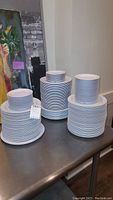 Three stacks of plates and bowls on a metal table, showing different sizes of plates and bowls with white and blue stripe design.