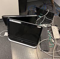 Two black HP Pavilion 20 All-in-One PCs stacked with multiple keyboards and a surge protector on carpeted floor.