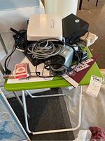 Wide shot showing all items resting on a green folding table including Adtran Bluesocket device, cables, scanner, markers, tape dispenser, pencil sharpener and playing cards.