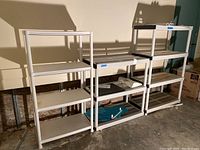 Full view of three white plastic shelving units placed side by side in a basement setting on concrete floor.