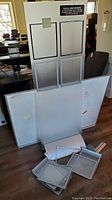Full view of disassembled metal presentation tower with four insert frames and multiple metal menu easels on floor in front.