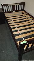Full view of twin bed frame showing wooden slats and footboard, dark brown finish with scratches.