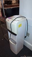 Full view of the white Primo water dispenser next to a black metal shelf.