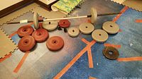 Barbell bar with multiple red and gray weight plates arranged on blue-orange foam floor mats.