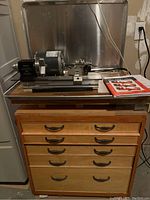 Taig lathe and GE motor mounted on top of wooden cabinet with manual laid beside them