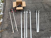 Overview of all clamps on driveway including 2 large Bessey bar clamps, 3 aluminum F-clamps, 2 Samona bar clamps and box of spring clamps