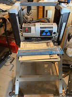 Front view of Delta portable planer mounted on its stand, with manual and blade pack on table