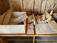 Overall view of various wooden jigs and fixtures on a table showing handmade wooden components, clamps, and a box