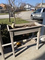 Photo showing one raised beige plastic garden planter with soil and a metal bunny decoration on top, with a metal turtle on the shelf below.