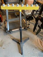 Front view of adjustable roller stand with yellow top and ball bearings on black tripod base