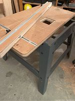 Photo showing metal stand with particleboard table and rectangular slot cut-out, includes adjustable fence with metal rails.