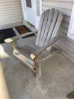 Close-up side view of one weathered wooden Adirondack chair on concrete porch.