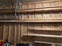 Multiple lengths of lumber and trim organized on wall-mounted metal shelves in a garage