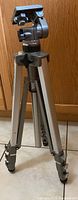 Full view of Velbon AEF-3 tripod standing on tile floor with adjustable head and extended legs.