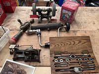 Wide view of entire collection on wooden workbench showing lathe, drill, grinding stone, tap and die set in wooden box, and decorative tin.