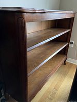 Dark stained wooden bookcase with three open shelves and curved legs