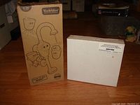 Two boxes: brown branded box for Yookidoo Flow N Fill Spout and plain white box for Light & Sound Piano, shown unopened