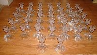 Overhead view of 37 clear glass/crystal candle stick holders arranged closely together on wooden floor showing uniform size and shape.