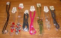 Overview photo of all eight necklace and earring sets displayed horizontally on a wooden surface, showing tags and various bead styles and colors.