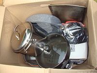 Box containing electric grill, multiple frying pans, large griddle, baking sheet, and a stainless steel stew pot with lid.