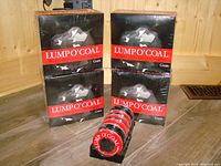 Four sealed rectangular boxes labeled Lump O Coal with four tins placed in front of them on a wooden floor.