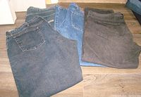 Four pairs of men's denim jeans, various colors and brands, folded on floor