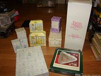 Overall view of 10 Precious Moments collectible figurines and doll in original boxes on a wooden table, showing variety of box shapes, sizes and designs.