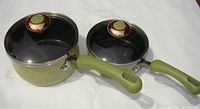 Two Paula Deen porcelain non-stick covered saucepans in pear speckle pattern on white background, showing green handles and glass lids with copper-green knobs.
