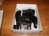 Black leather ankle boots inside white Regarde LeCiel branded box, showing zipper detail and slight creasing on leather.