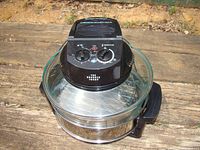 Side view of the halogen oven with glass bowl and control unit showing the whole appliance on wooden background.