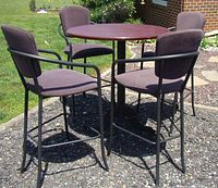Full set showing round table with four cushioned armchairs on black metal frames outdoors on gravel