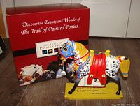 Horse figurine in front of its red branded box, showing figurine and packaging.