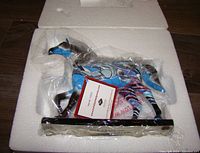 Horse figurine in plastic wrap inside white foam packaging with a certificate card.