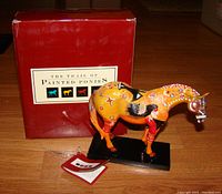Painted resin horse figurine with box and certification tag displayed on wooden floor.