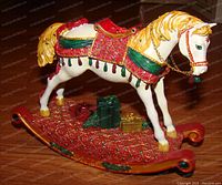 Photo of the Noel Christmas Rocking Horse figurine, showing detailed decorations on the rocking base and horse in red, green, gold and white color scheme with gifts present.