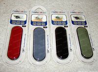 Four Momo Stick universal cell phone finger grip straps in original packaging. Colors: red, blue-gray, black, green.