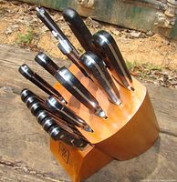 Full view of signed wooden knife block holding knives with black handles and scissors.